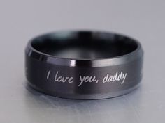 i love you, daddy engraved on the inside of a black wedding ring with white lettering