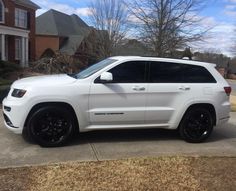 a white jeep parked in front of a house on a driveway with black rims