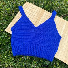 a blue knitted sweater laying on top of a wooden board next to green bushes