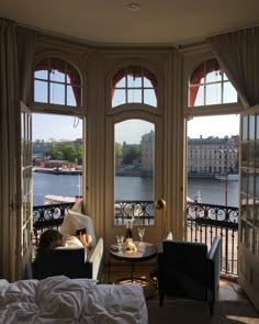 a woman sitting in a chair looking out at the water from a room with large windows