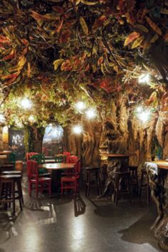 the interior of a restaurant with many tables and stools covered in leaves hanging from the ceiling