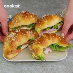 sandwiches with ham, lettuce and cheese being held by two hands over a plate