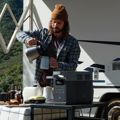 a man pouring something into a cup on top of a table next to a truck