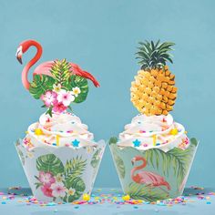 two cupcakes with pineapples and flamingos on them are sitting next to each other