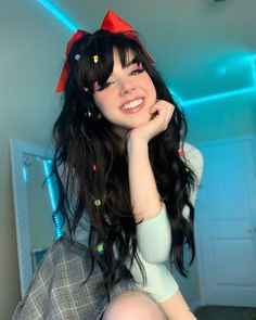 a woman with long black hair wearing a white shirt and red bow sitting on top of a bed