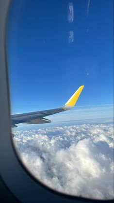 the wing of an airplane flying over clouds and blue sky with bright yellow tail fin