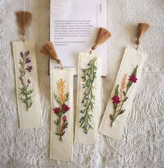 four embroidered bookmarks with flowers and leaves on them sitting on a white tablecloth