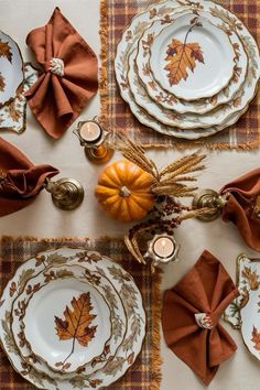 the table is set for thanksgiving dinner with plates and napkins, candles, and pumpkins