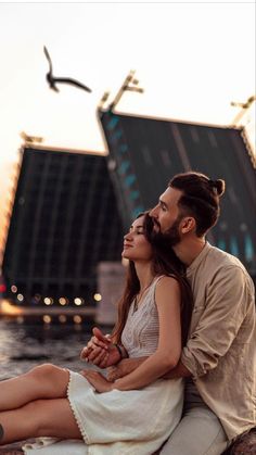 a man and woman sitting next to each other in front of a body of water