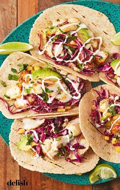 four tacos on a blue plate with lime wedges and cilantro sauce