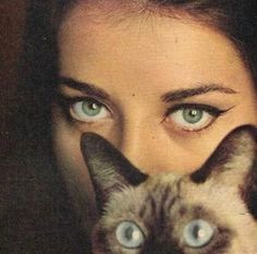 a woman with blue eyes is holding a siamese cat up to her face while looking at the camera