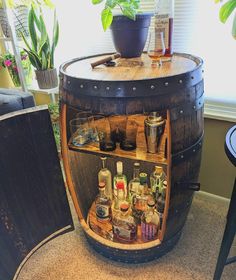 a wooden barrel filled with liquor bottles and glasses sitting on top of a table next to a potted plant