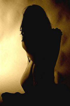 the silhouette of a woman holding a cell phone in front of a light that is behind her