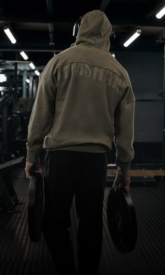 a man in a hoodie carrying two dumbbells while standing on a gym floor