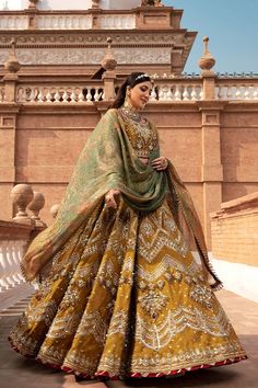 a woman in a yellow and green lehenga is standing on the ground with her hands behind her back