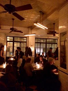 a group of people sitting at tables in a room with ceiling fans and lights on the walls