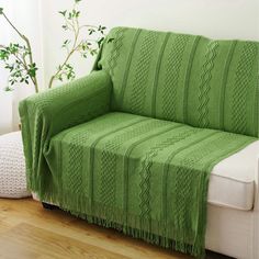 a green blanket sitting on top of a white couch next to a potted plant