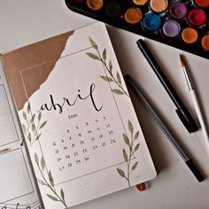 an open calendar sitting on top of a desk next to markers and paintbrushes