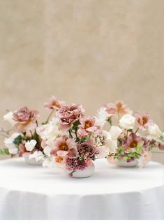 three white vases with pink and white flowers in them on top of a table