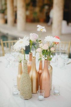 three vases filled with flowers sitting on top of a white table covered in glasses