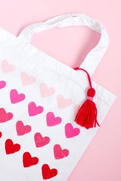 a white bag with hearts painted on it and a tassel hanging from the handle