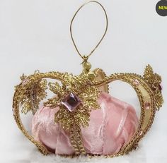 a pink and gold tiara is sitting on a white surface, with an ornament hanging from the crown