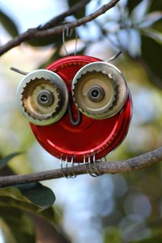 an owl shaped object hanging from a tree branch with eyes made out of metal parts