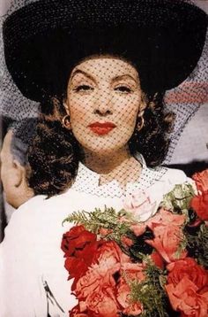 a woman wearing a black hat and holding flowers