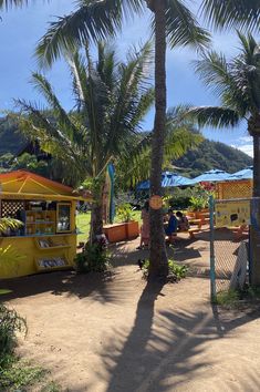 a yellow food truck parked next to palm trees and people sitting at tables under umbrellas