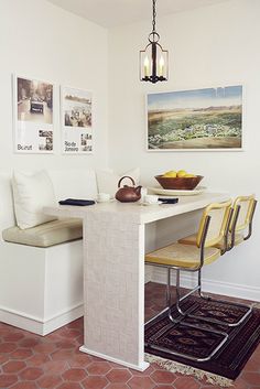 a white table with two yellow chairs and a bowl of fruit on the counter next to it