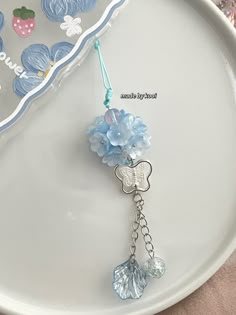 a white plate topped with a blue flower and butterfly keychain hanging from it's side