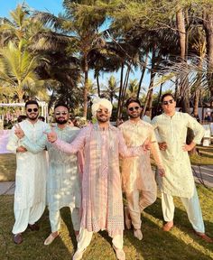 four men in white and pink outfits posing for the camera with palm trees behind them