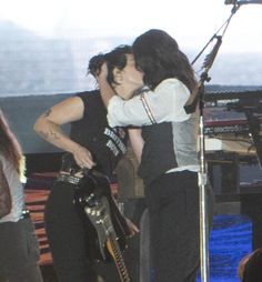 two people are kissing on stage while one person is holding a guitar and singing into a microphone