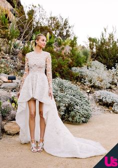 a woman in a wedding dress standing on a dirt road with bushes and rocks behind her