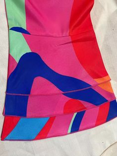 a colorful dress is laying on a white sheet with blue, pink, and green designs