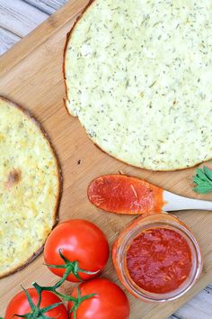 two pizzas and tomatoes on a cutting board