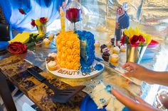 a person is decorating a cake on a table with flowers and other decorations around it