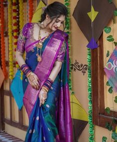 a woman in a purple and blue sari standing next to a wall with decorations