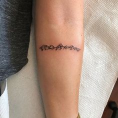 a woman's arm with a tattoo on it that has mountains in the middle