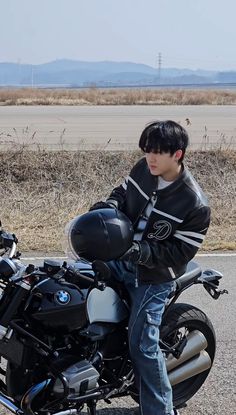 a young man sitting on the back of a black and white motorcycle in front of a field