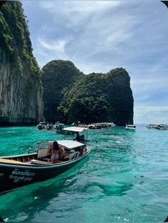 several boats floating in the water near some cliffs and small islands with people on them