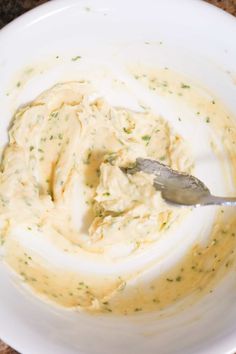 a white bowl filled with cream sauce and a spoon in it on a brown table