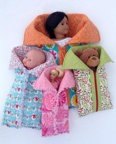 three dolls are laying next to each other in blankets and sleeping bags on the floor