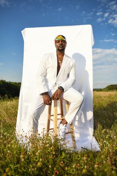 a man sitting on top of a wooden stool in the middle of a grass covered field