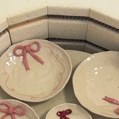 four plates with pink bows on them sitting on a counter top in front of a brick wall