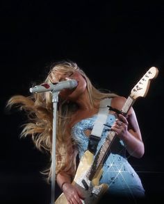 a woman holding a guitar and singing into a microphone