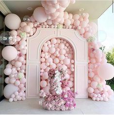 a cake surrounded by balloons in front of a wall with an arch and flowers on it