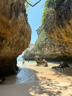 people are walking on the beach near large rocks