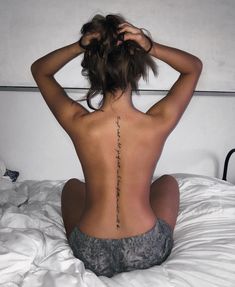 a woman sitting on top of a bed with her back turned to the camera and tattoos