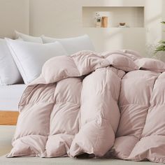 an unmade bed with pink comforter and pillows on the floor next to a potted plant